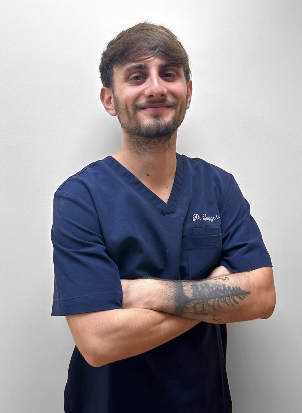 Ritratto di Riccardo Di Lazzaro, fisioterapista e osteopata, in camice blu e a braccia conserte